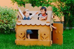 Deux enfants jouent dans une maisonnette en bois installée dans un jardin.